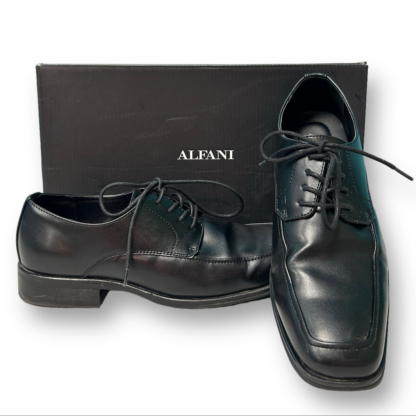 A pair of black Alfani men's dress shoes placed in front of a black Alfani branded box.