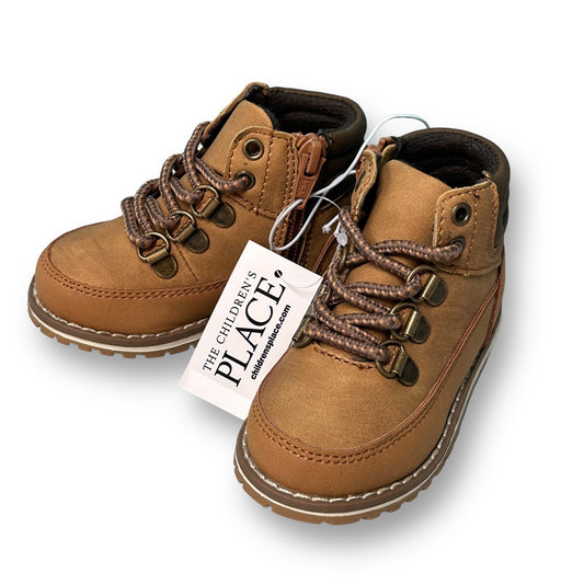 A pair of tan leather-style boots for toddlers boys with lace-up closure and a brand tag attached.