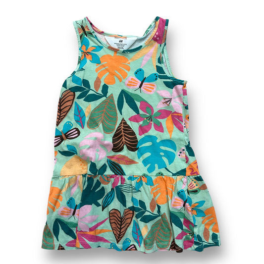 A sleeveless cotton dress for girls with a green tropical print, featuring a variety of colors and leaf patterns.