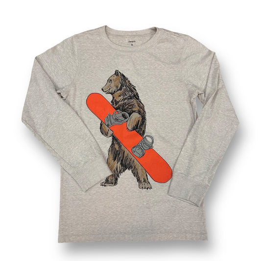 A long sleeve tan shirt with a graphic of a bear riding a snowboard, with red and silver details on the board.