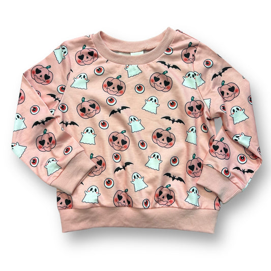 A pink sweatshirt with a halloween print featuring ghosts, pumpkins, and bats.