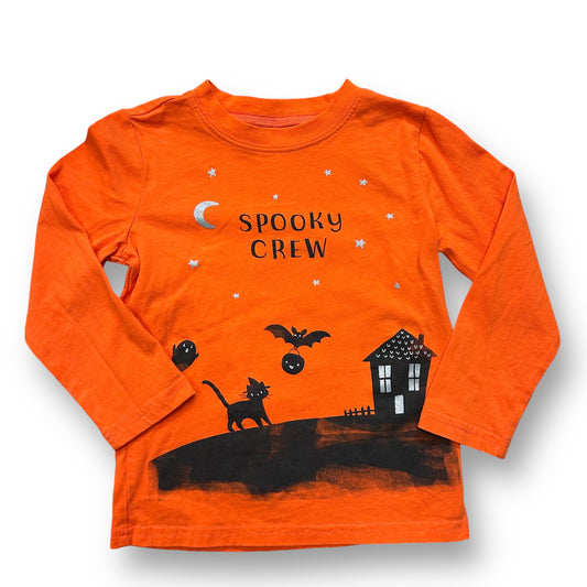 An orange long-sleeve Carter's shirt with 'Spooky Crew' text and Halloween-themed illustrations including a bat, pumpkin, and a haunted house.