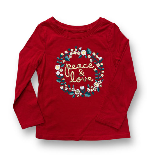 A red long-sleeved girls' top with 'PEACE & LOVE' text and Christmas-themed decorations like snowflakes, ornaments, and flowers on it.