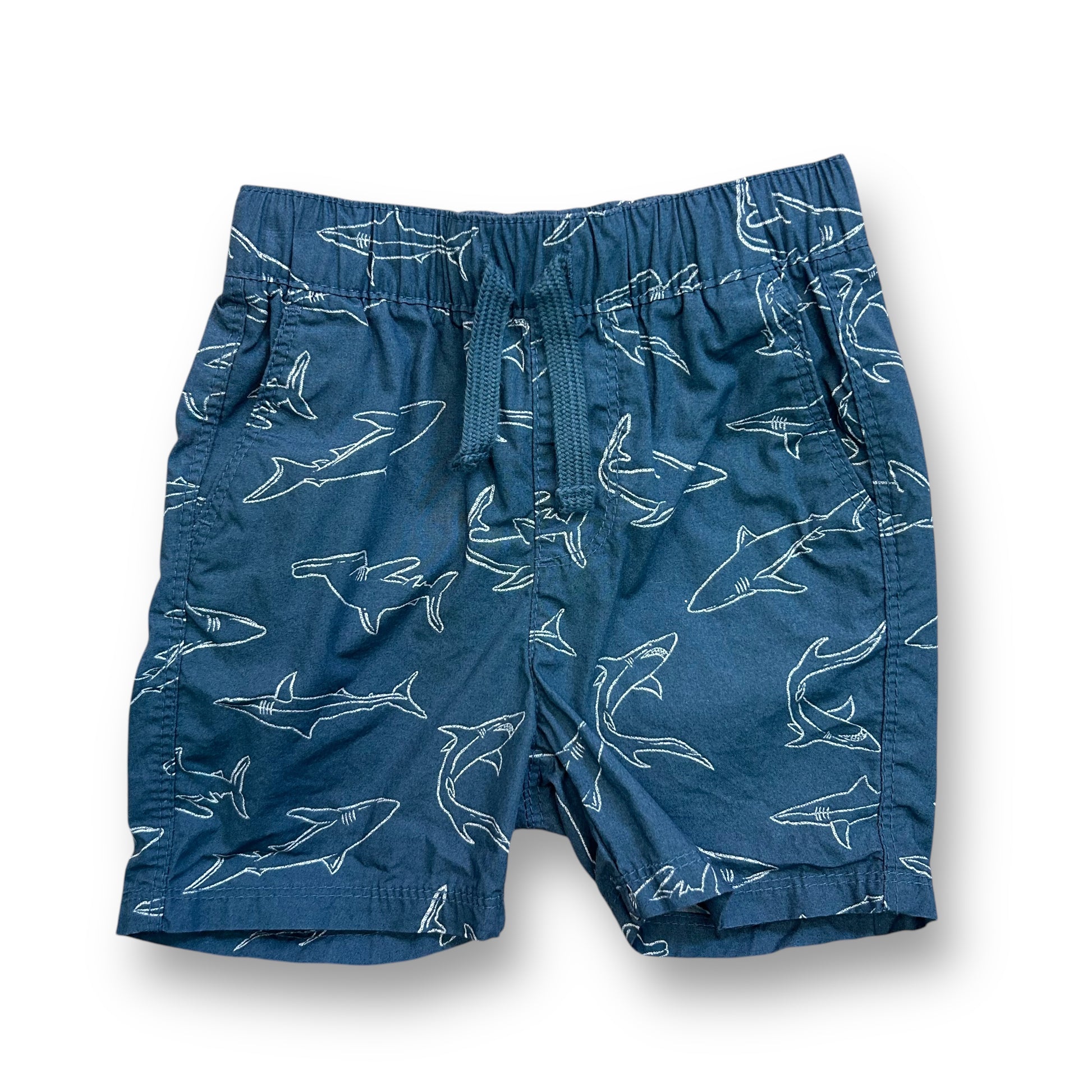 A pair of blue shorts with a shark print, designed for toddlers.
