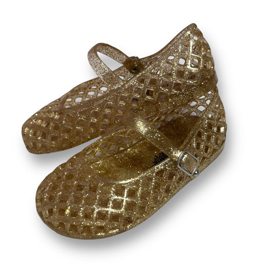A pair of gold shimmering toddler girl sandals with a buckle closure.