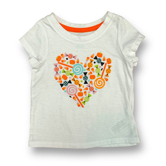 A white short-sleeved girls' shirt with a heart-shaped design featuring multicolored candy corn patterns.